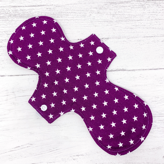 Large reusable sanitary towel or cloth pad in purple cotton fabric with white star pattern. Back view.