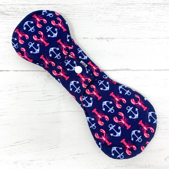 Reusable cloth sanitary pad with navy lobster and anchor pattern. Reverse of pad shown fastened.