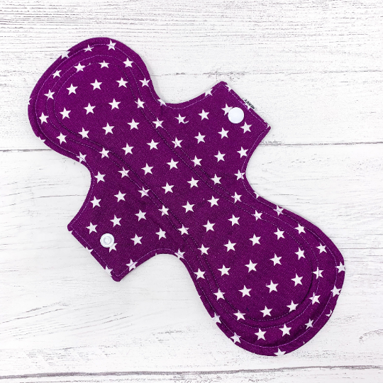 Large reusable sanitary towel or cloth pad in purple cotton fabric with white star pattern. Front view. 