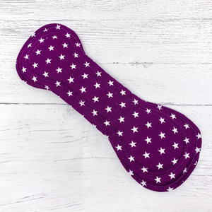 Large reusable sanitary towel or cloth pad in purple cotton fabric with white star pattern. Front view of fastened pad.