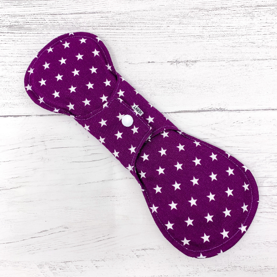 Large reusable sanitary towel or cloth pad in purple cotton fabric with white star pattern. Back view of fastened pad. 