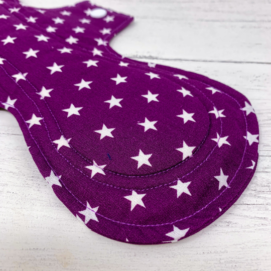 Large reusable sanitary towel or cloth pad in purple cotton fabric with white star pattern. Close up view of stitching.