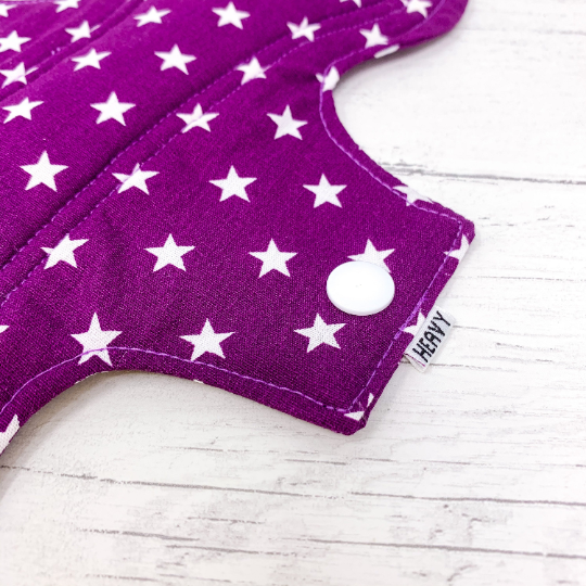 Large reusable sanitary towel or cloth pad in purple cotton fabric with white star pattern. Close up view of fastening.