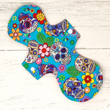 Load image into Gallery viewer, Reusable cloth sanitary pad with bright blue sugar skulls pattern. Reverse side shown.
