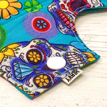 Load image into Gallery viewer, Reusable cloth sanitary pad with bright blue sugar skulls pattern. Close up view of fastening.
