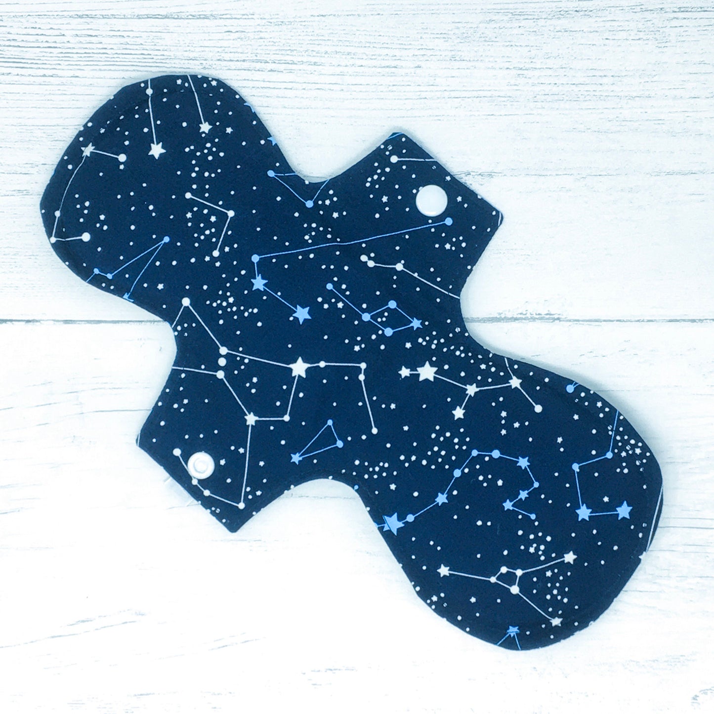 11" Reusable menstrual pad with pattern of constellations on a navy cotton fabric. Reverse side shown