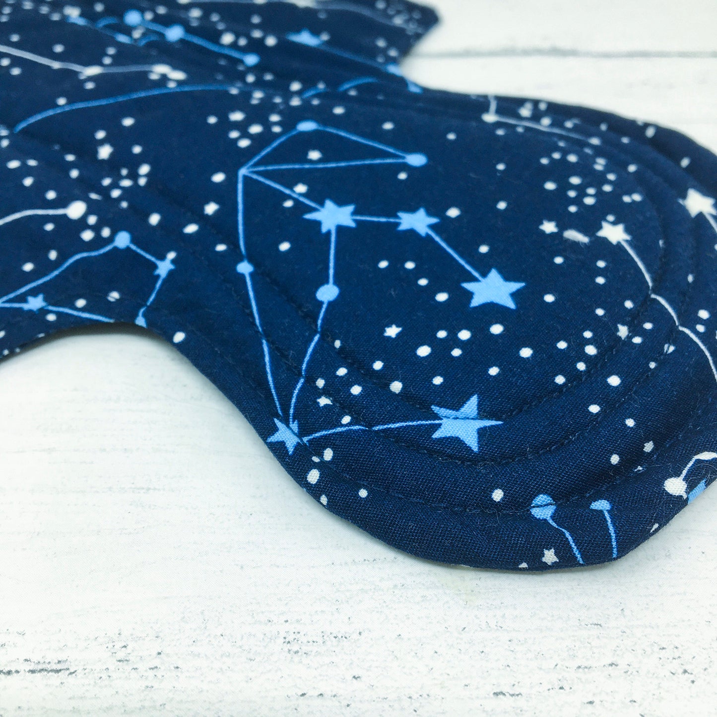11" Reusable menstrual pad with pattern of constellations on a navy cotton fabric. Close up view of stitching